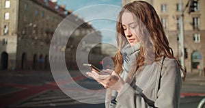 Attractive brunette young woman texting on phone while standing on a city street.