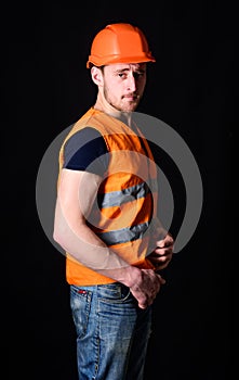 Attractive builder concept. Builder in helmet posing confidently. Man in helmet, hard hat wears orange vest, black