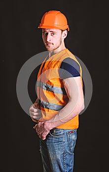 Attractive builder concept. Builder in helmet posing confidently. Man in helmet, hard hat wears orange vest, black