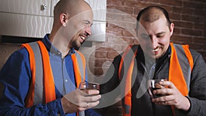 Attractive builders are drinking coffee on a break. They are talking and smiling.