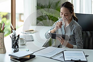 Attractive business asian woman using a digital tablet while sitting in workplace desk in an office.