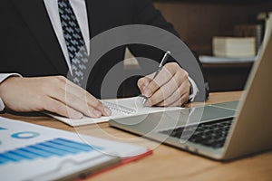 Attractive business man in black suit working and writing on document report on desk in meeting room