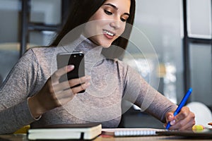 Attractive business woman sits at table in front of laptop, makes notes in notebook, draws up business schedule.