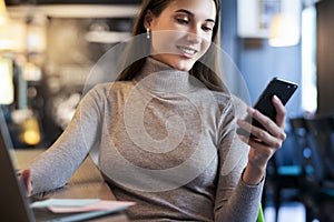 Attractive business woman sits at table in front of laptop and talks on mobile phone, negotiates on the phone.