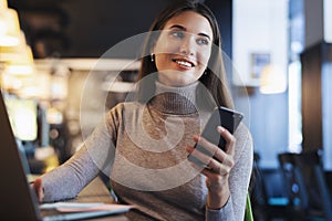 Attractive business woman sits at table in front of laptop and talks on mobile phone, negotiates on the phone.