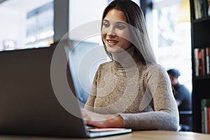 Attractive business woman sits at table in front of laptop, works remotely while in cafe.