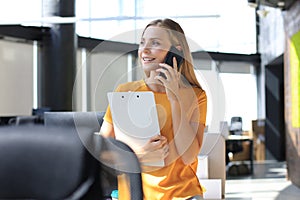 Attractive business woman talking with collegues on the mobile phone while sitting on the office desk