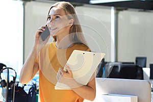 Attractive business woman talking with collegues on the mobile phone while sitting on the office desk
