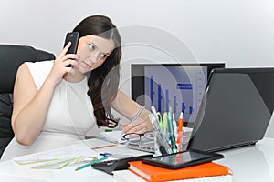 Attractive business woman use smart phone and sitting at her worktable with documents and electronic devices