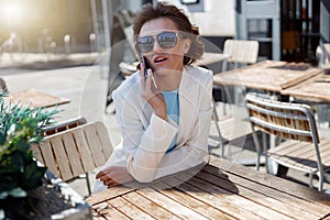 Attractive business woman in white suit sitting in cafe and talking phone