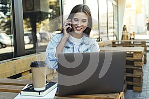 Attractive business woman working in cafe on open terrace, sitting in front of laptop, talking on the phone.