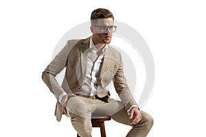 Attractive businessman with glasses sitting on wooden chair and looking away