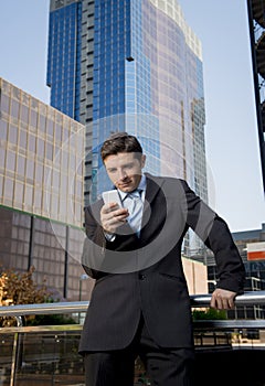 Attractive businessman looking text message at mobile phone outdoors