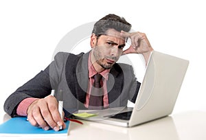 Attractive businessman at office desk working on computer laptop looking tired and busy