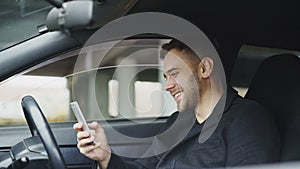 Attractive businessman sitting inside car laughing while using smartphone after trip