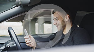 Attractive businessman sitting inside car laughing while using smartphone after trip