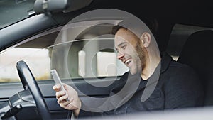 Attractive businessman sitting inside car laughing while using smartphone after trip