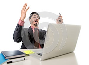 Attractive businessman sitting at office desk working in stress on computer laptop talking on mobile phone overworked