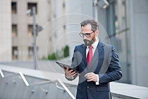 Attractive businessman in suit and red tie check or read digital tablet outdoor office building. Social communicate technology