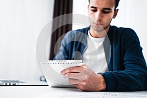 Attractive businessman working at office on laptop and notepad while sitting at table