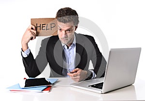 Attractive businessman working in stress at computer holding help cardboard sign