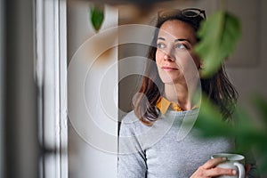 Attractive businesswoman with coffee standing indoors in office, resting.