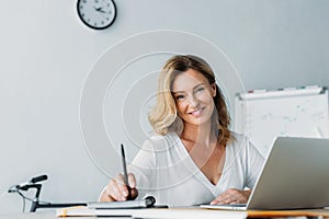 attractive businesswoman holding pen and looking at camera