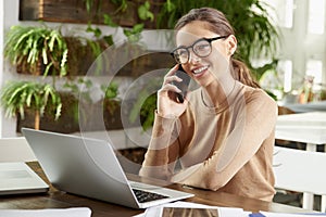 Attractive businesswoman making a call while sitting in front of laptop in the office and working