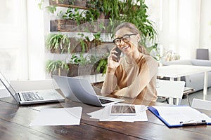 Attractive businesswoman making a call while sitting in front of laptop in the office and working