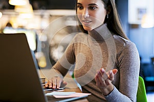 Attractive businesswoman sitting at a table in front of a laptop and using video chat for work.