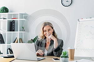 attractive businesswoman sitting at table with laptop and looking at camera