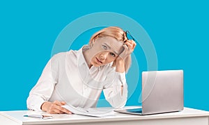 Attractive businesswoman tired of computer work sitting at her desk over blue studio background, panorama