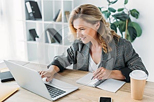 attractive businesswoman using laptop and writing something to notebook