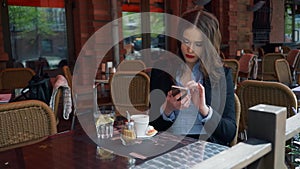 Attractive Businesswoman wearing Suit using Smartphone in an outdoor Cafe, drinking Coffee. SLOW MOTION. Professional