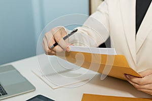 Attractive businesswoman in white suit hand open business report from document envelope and working on desk in meeting room