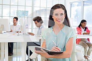 Attractive businesswoman writing in notebook and smiling to camera