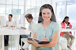 Attractive businesswomen writing in notebook with colleagues behind her