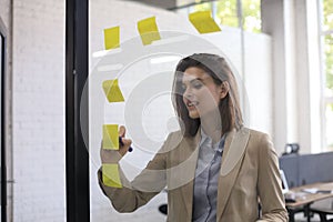 Attractive busness woman post stickers on glass at office and writing on them