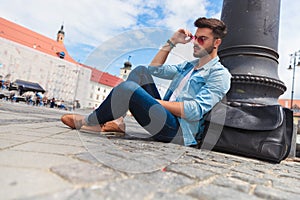 Attractive casual man sitting in the city fixes red sunglasses