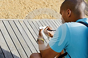 Attractive casually dressed young american african hipster man making notes in copybook. Student preparing for lesson at