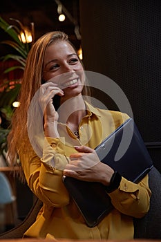 attractive cauasian woman calling by smartphone, holding laptop in hands at cafe photo