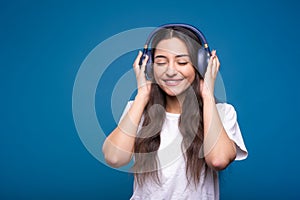 Attractive caucasian or arab brunette girl in a white t-shirt listening to her favorite music on headphones isolated on a blue stu