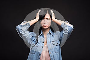 Attractive caucasian brunette girl in a shirt touching her head with her hands because of a headache isolated on a black studio ba