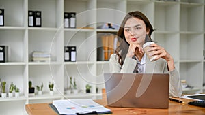 Attractive caucasian businesswoman sipping coffee, looking out the window, sitting at desk
