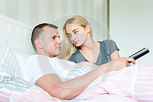 Attractive caucasian couple in bed. Man watching tv, woman lovingly looking at him, hoping to catch his attention.