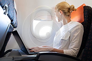 Attractive caucasian female passenger looking through the plain window while working on modern laptop computer using