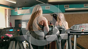 Attractive caucasian girl runs on a treadmill in the gym. back view