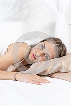 Attractive Caucasian girl in silk lingerie sleeps on a beauty pillow on a white bed in the bedroom