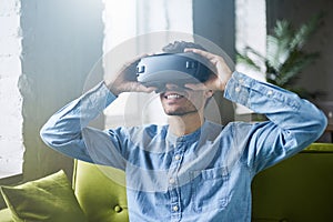 Attractive caucasian man in denim shirt and vr headset sitting on green sofa at home