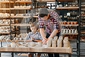 Attractive caucasian man and liitle cute boy kneading clay for pots.